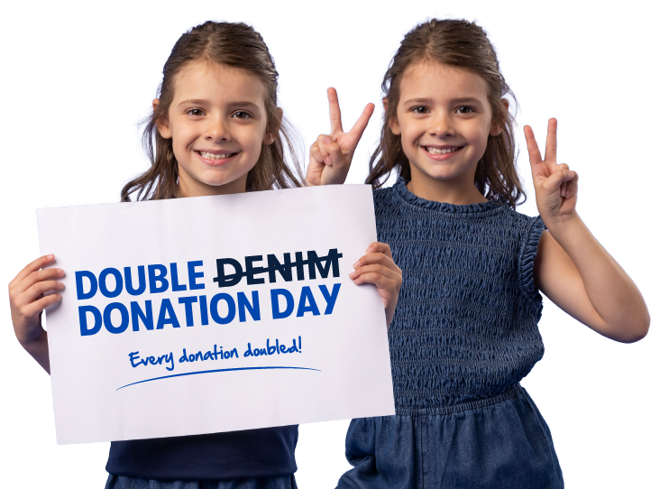 Two young girls smiling and holding up peace signs, one holding a sign that reads 'Double Denim Donation Day, every donation doubled'